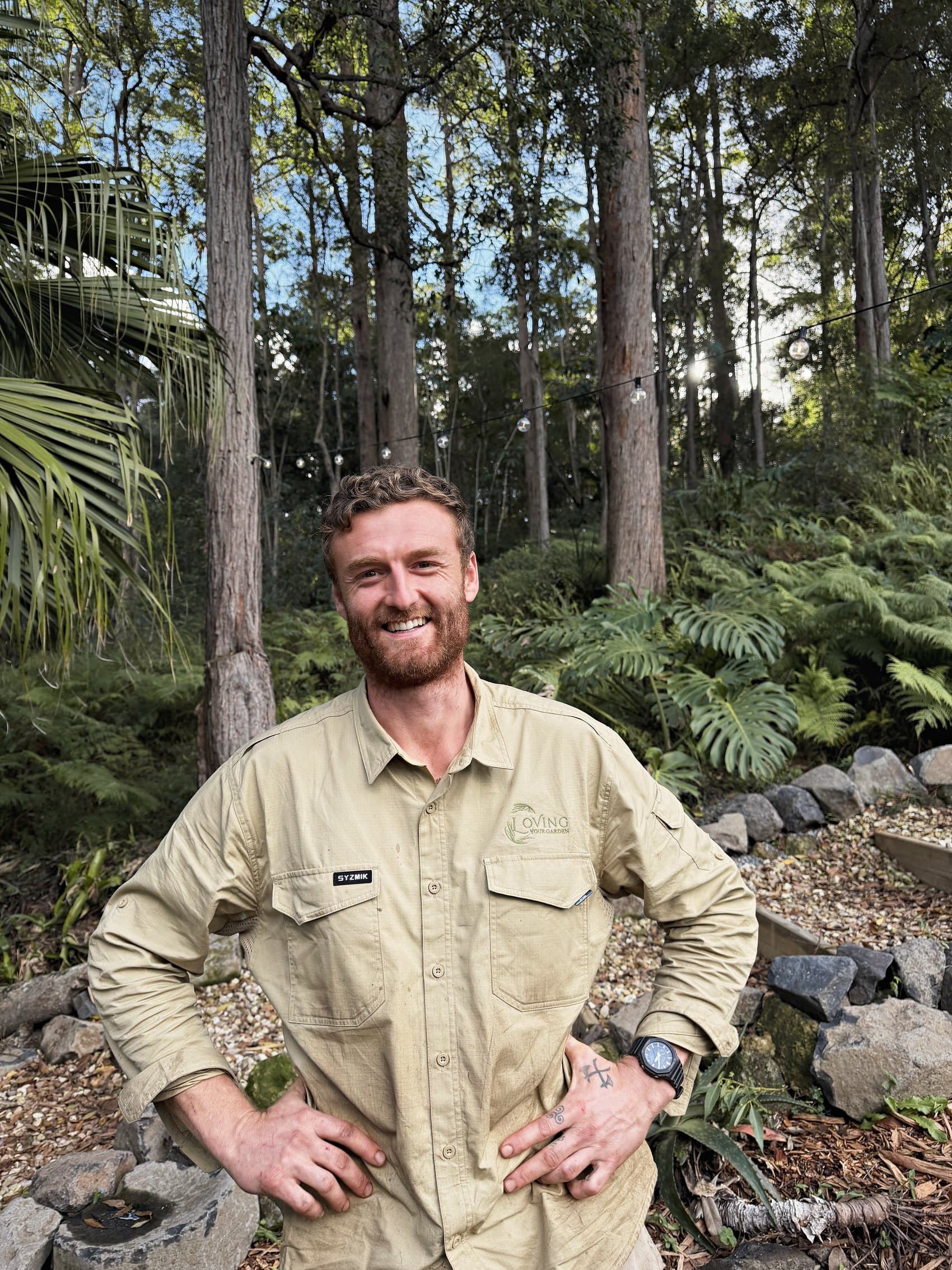 Chris Dowsett smiling in a garden he cares for, eucalypts and tree ferns behind